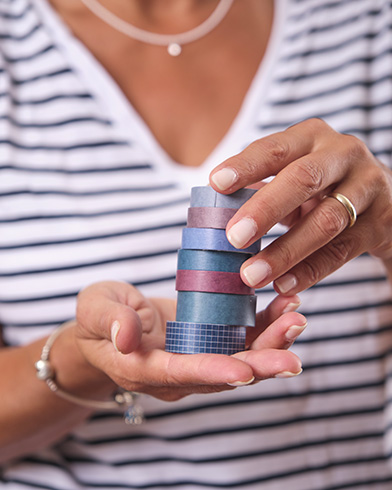 LAGRAFICALEGGERA_WASHI-TAPE Il particolare delle mie mani mentre tengo una pila di washi tape colorati dall'azzurro al melanzana